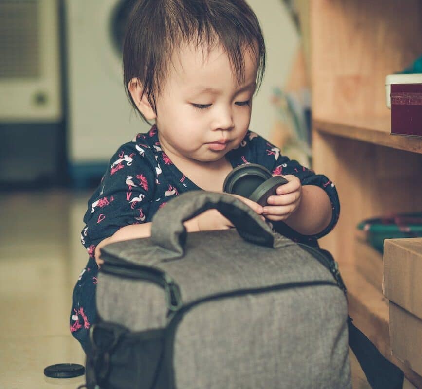 baby girl playing with a camera bag on an apartment floor