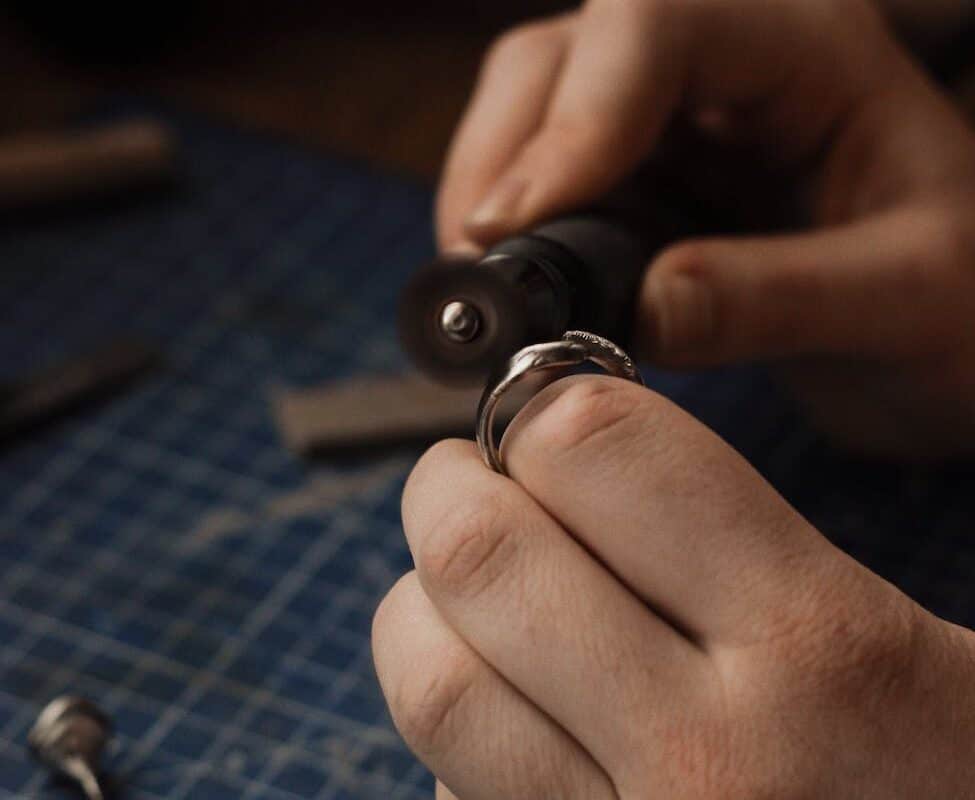 person holding a silver ring and a jewelry grinder
