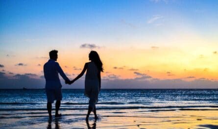 man and woman holding hands walking on seashore during sunrise