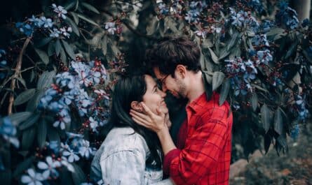 man holding woman s face beside blue cluster flowering plant