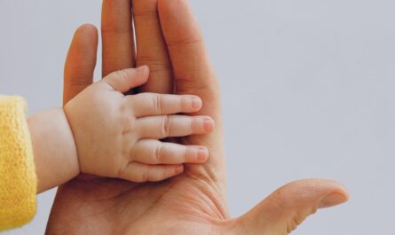 crop person touch palms with newborn baby on gray backdrop