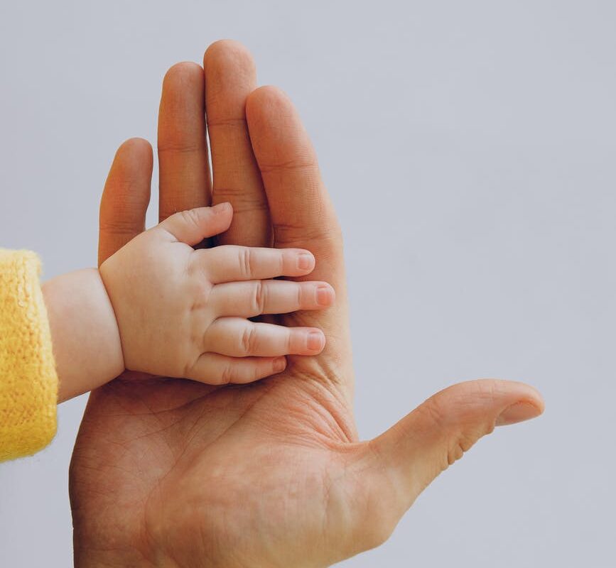 crop person touch palms with newborn baby on gray backdrop